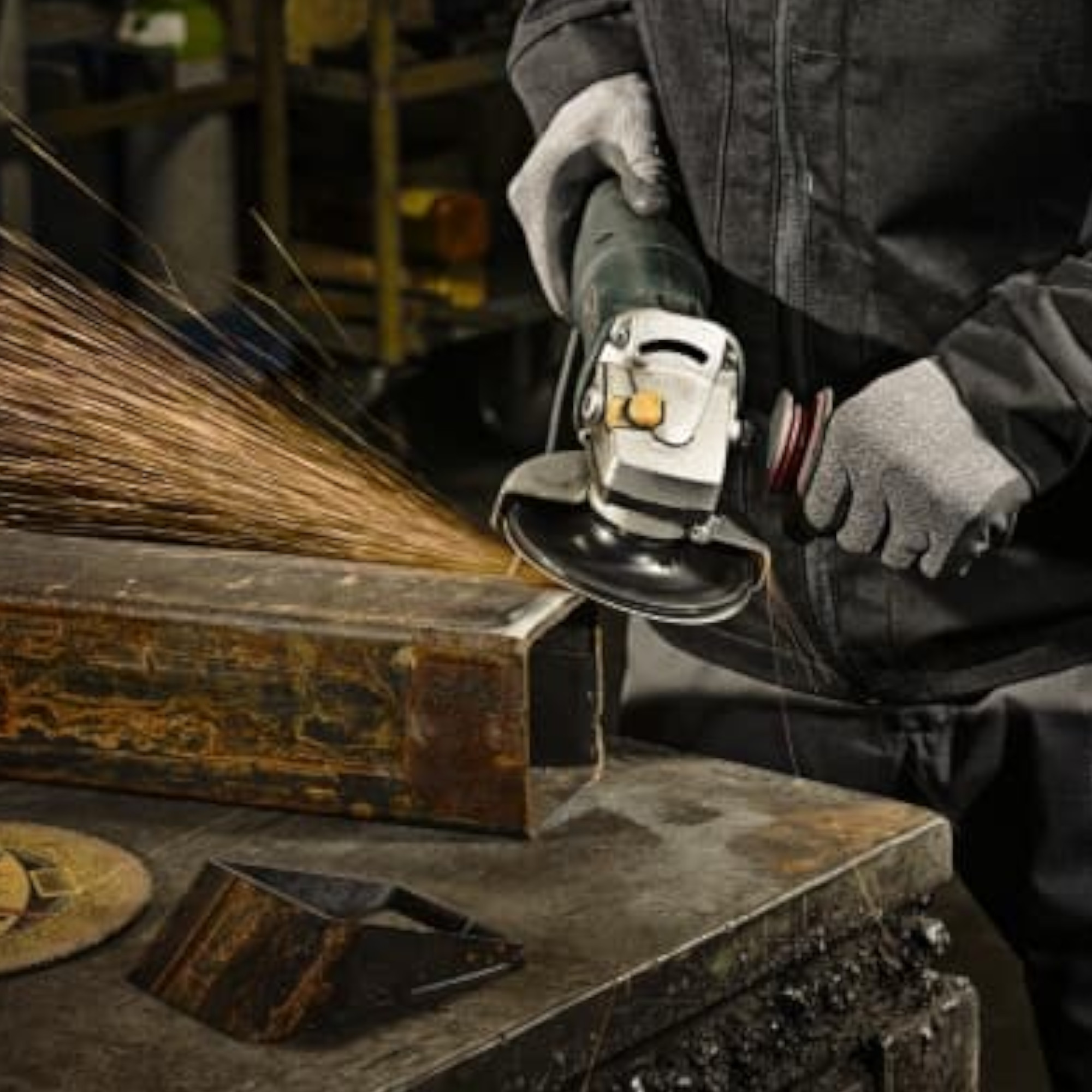 Ein Handwerker hält eine Winkelschleifmaschine und bearbeitet ein Metallstück. Funken fliegen aus dem Schleifwerkzeug, während er mit geschützten Händen arbeitet. Im Vordergrund befinden sich Metallteile auf einer Werkbank.