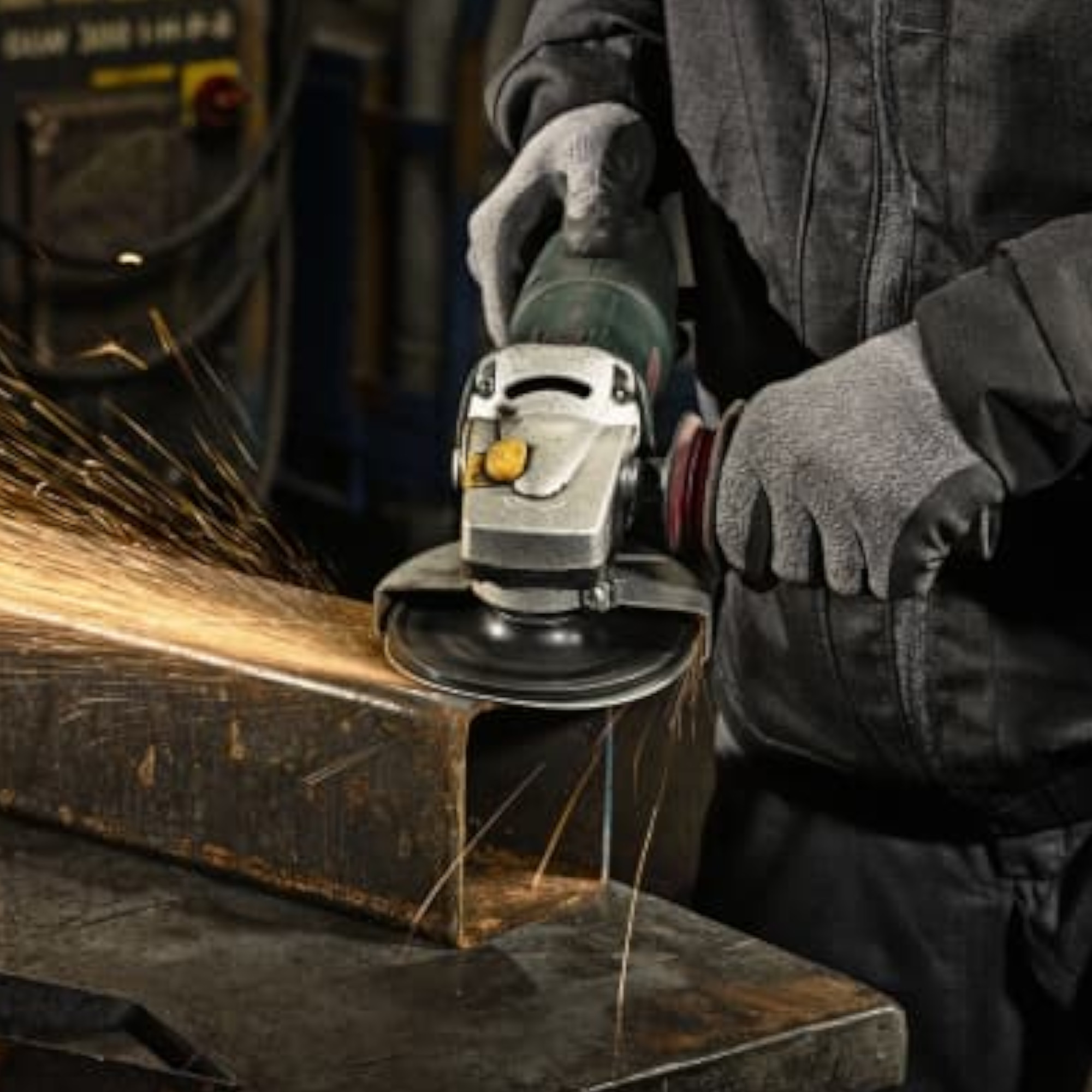 Ein Arbeiter nutzt einen Winkelschleifer, um ein Metallstück zu bearbeiten. Funken fliegen aus dem Gerät, während er mit einem Handschuh geschützt die Maschine führt. Der Hintergrund zeigt eine Werkstatt.